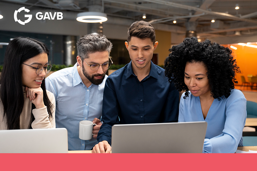 Quatro pessoas em um ambiente corporativo moderno trabalham juntas em frente a um laptop, analisando informações na tela com expressões atentas e colaborativas.