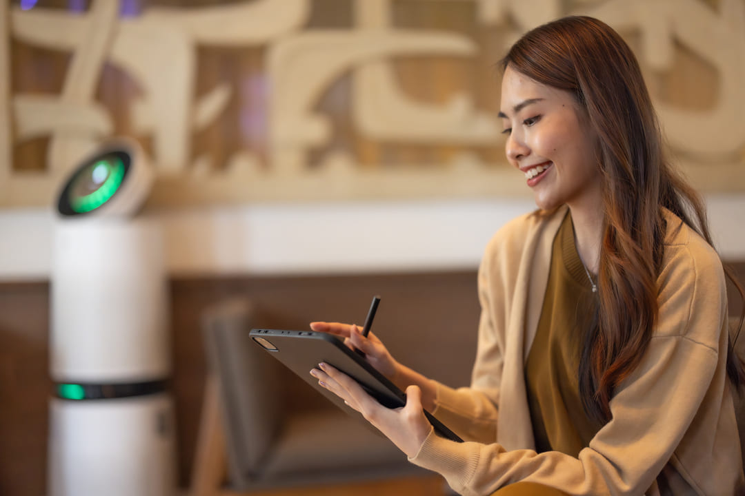 Mulher interagindo com tablet digital em ambiente moderno com presença de robô assistente, simbolizando o uso de chatbots inteligentes.