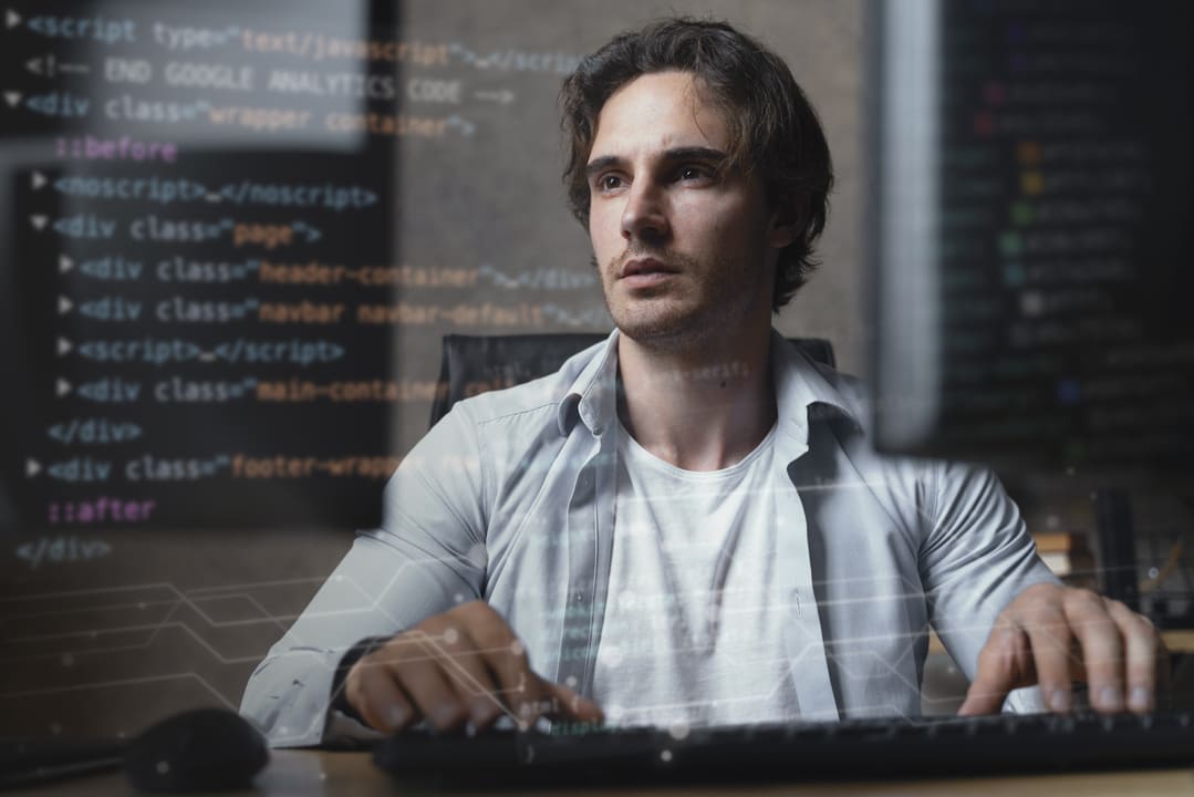 Homem concentrado trabalhando em um computador, com códigos de programação projetados sobre a imagem.