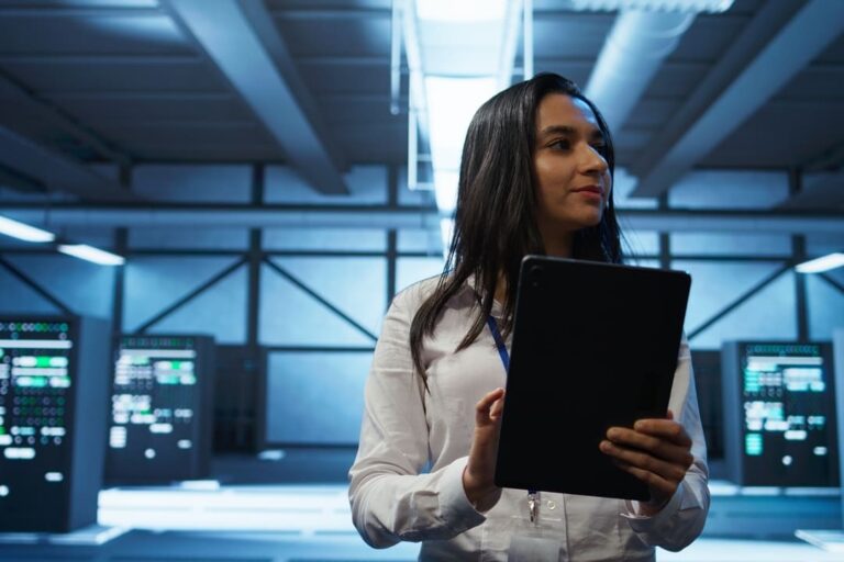 Mulher segurando um tablet em um data center, representando o uso de tecnologias baseadas em nuvem.
