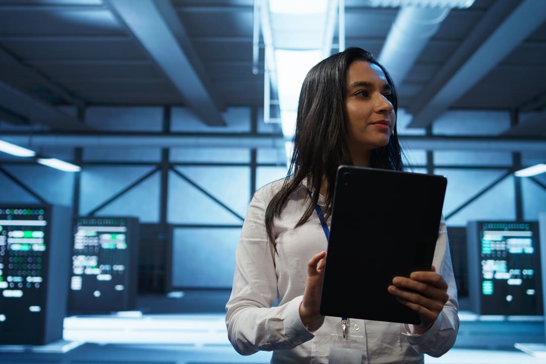 Mulher segurando um tablet em um data center, representando o uso de tecnologias baseadas em nuvem.