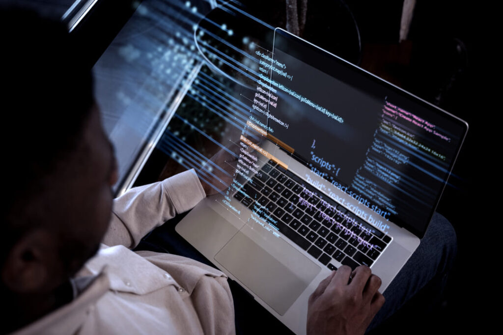 Homem visto de cima digitando em laptop com códigos de programação projetados, simbolizando outsourcing de TI.