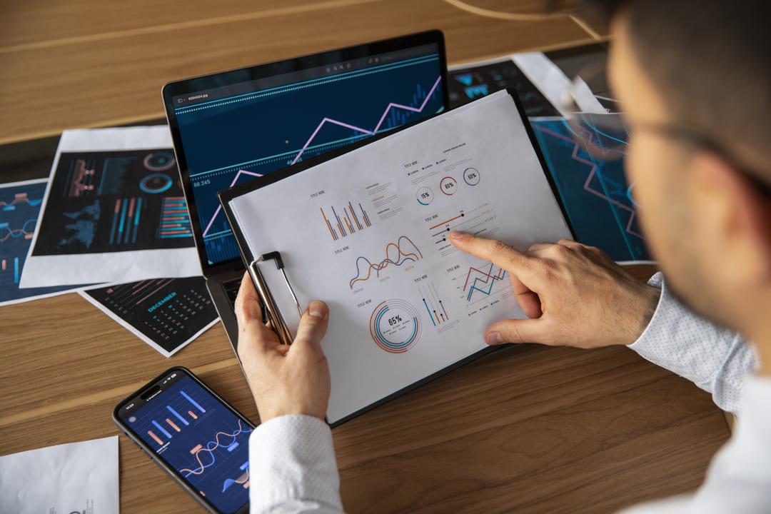 Profissional analisando gráficos e relatórios em um tablet e computador para análise preditiva de dados.