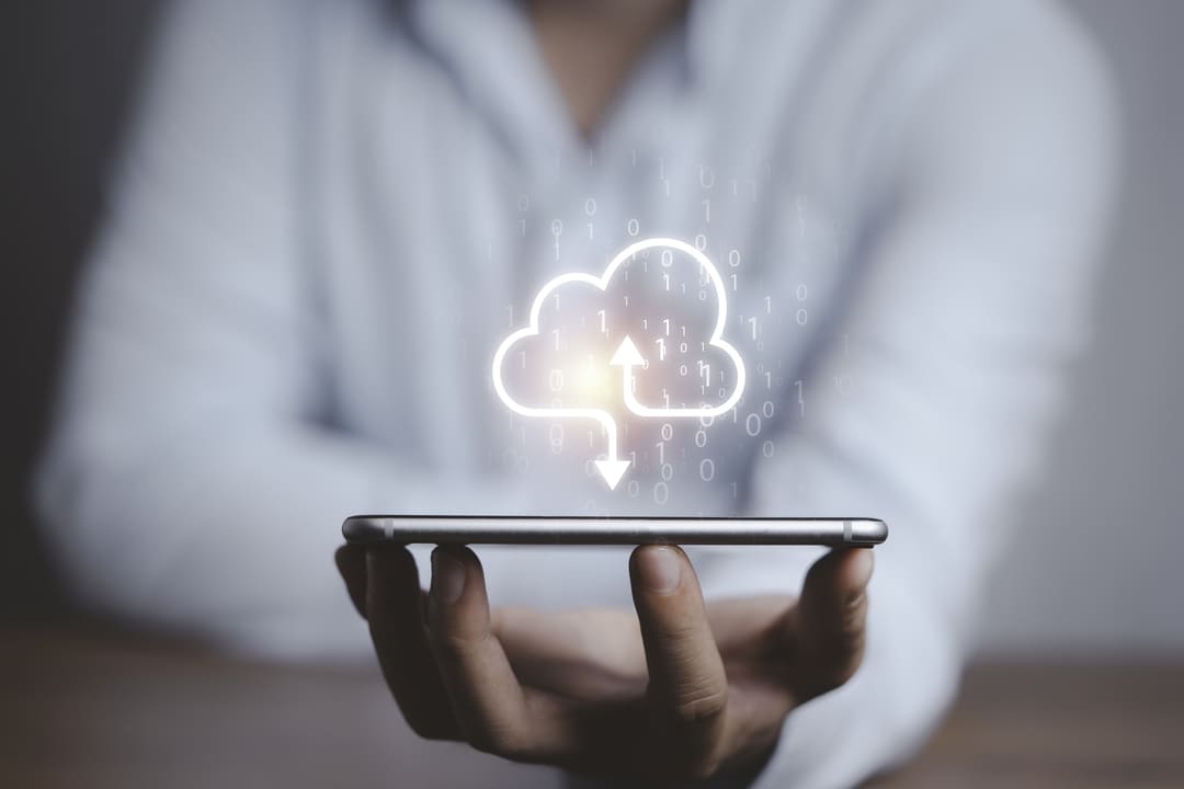 Computação em nuvem representada por ícone de nuvem com setas de upload e download sobre um smartphone.