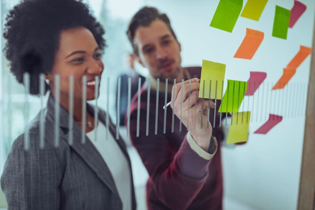 Profissionais planejando estratégias com post-its coloridos em um painel transparente durante uma reunião de análise de dados.